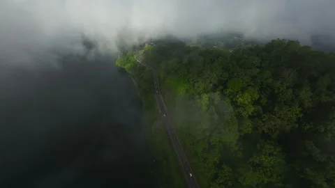 Fpv drone falling through the clouds into a road with green hills &amp; lake 스톡 동영상 259774780