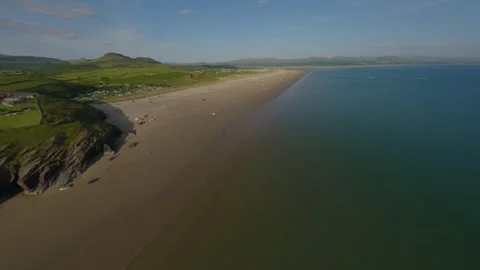 FPV Drone flies past cliffs at the beach with Snowdonia mountain background Stock Footage 242449697