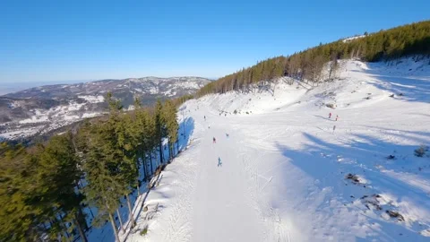 FPV drone flight over snowy ski slope with skiers and mountain view on sunny day Video stock 337494065