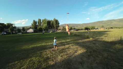 FPV drone flying through swing set and following boy on zipline at sunset Stock Footage 248161987