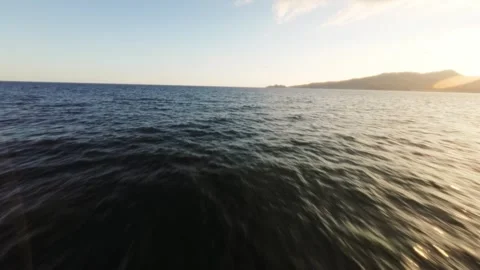 FPV drone gliding above ocean during golden hour with sunset and distant Stock Footage 310666232