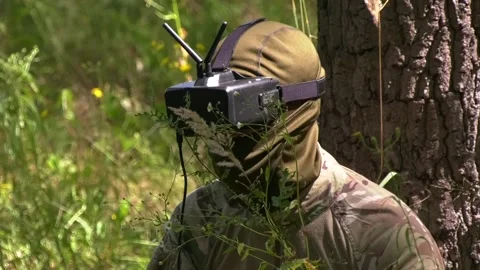 An FPV drone operator sits on a lawn near a tree and controls the drone. Stock-Footage 346518076