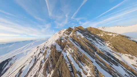 FPV drone soars over the ridges of a snow-covered mountain during a sunset Stock Footage 253555687