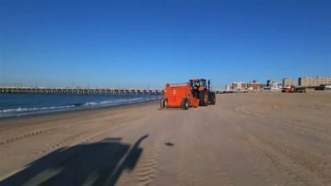 FPV drone view of orange tractors with rakes cleaning the beach at Coney Island Stock Footage 310596313
