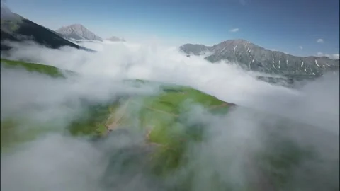 FPV flight through clouds over green hills and mountains under blue sky Stock Footage 341358049