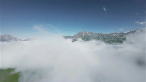 FPV flight through clouds revealing mountains and blue sky in serene landscape Stock Footage 341357879