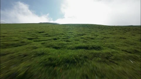 FPV low flight over lush green hillside with clouds and blue sky above Stock Footage 341358061