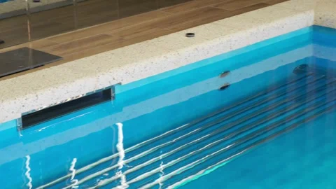 A fragment of an indoor overflow pool with clear blue water and a metal bench. E Stock Footage 312076920