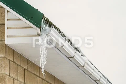 Fragment of roof cornice with overhang icy icicle gutter after thaw Stock Photos