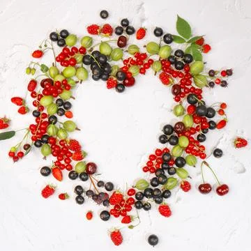 Frame of assorted berries in shape of heart on white background. Copy space. Stock Photos
