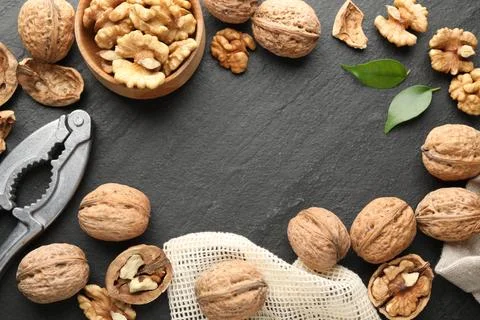Frame of fresh ripe walnuts, shells and nutcracker on black table, flat lay Stock Photos