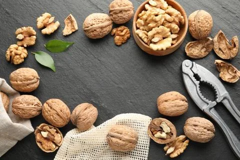 Frame of fresh ripe walnuts, shells and nutcracker on black table, flat lay Stock Photos