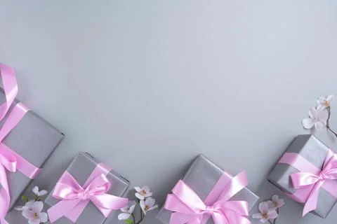 Frame of gray gift boxes with pink bows and flowers on light gray background. Stock Photos