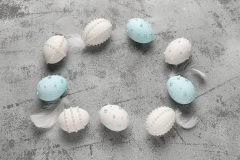 Frame made of Easter eggs decorated with pearls and feathers on grey grunge b Stock Photos