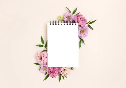 Frame made of eustoma flower and blank notepad mockup on a beige background. Stock Photos