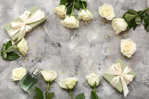 Frame made of gift boxes, white rose flowers and bottle of perfume on grey gr Stock Photos