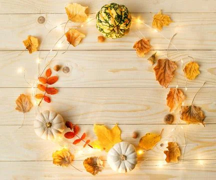 Frame made of pumpkins, lights, dried leaves on wood background. Stock Photos