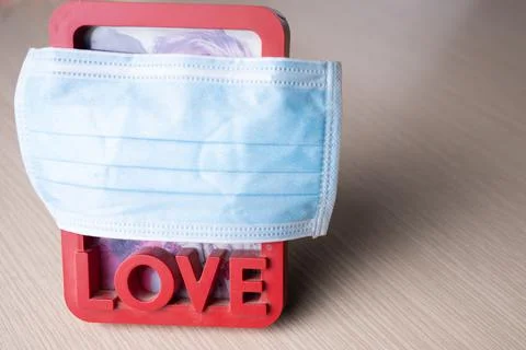 A frame with a photo of a young couple in love is covered with a medical mask Stock Photos