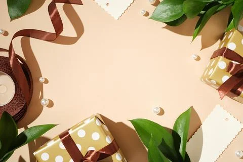 Frame of polka dot gift boxes, brown ribbons, leaves, and tags on a beige bac 库存照片