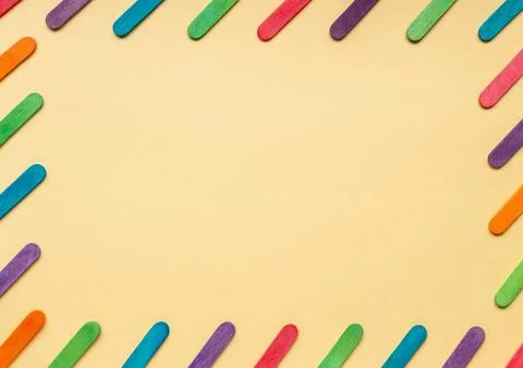 Frame with tilt multicolored rounded flat sticks on a peach-colored background. Stock Photos