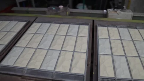 Framed sheets of glossy white tiles travel along a long conveyor past a wall Vídeo Stock 346737654