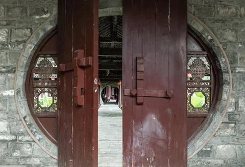 Framed by a weathered grey stone wall, a traditional Chinese moon gate stan.. Stock Photos