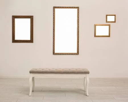 Frames with empty canvases on wall and bench in modern art gallery. Mockup fo Stock Photos