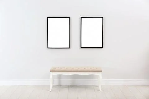 Frames with empty canvases on wall and bench in modern art gallery. Mockup fo Stock Photos