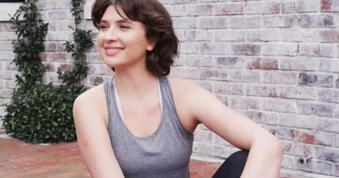 Frames showing woman drawing knee toward chest on yoga mat outdoors turning head Stock Footage 335624618