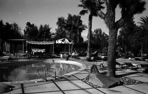Frank Sinatra sitting outside on the pool deck of his Palm Springs home, reading Stock Photos