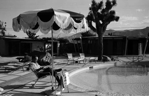 Frank Sinatra sitting outside on the pool deck of his Palm Springs home, reading Stock Photos