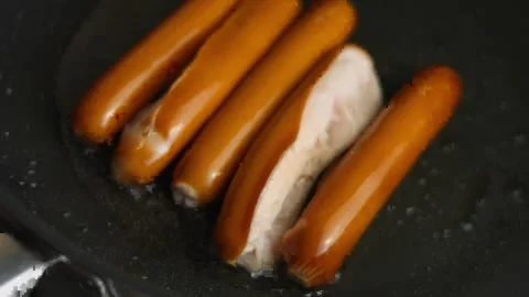 Frankfurter sausages being fried, two sausages have split open Stock Footage 329054928