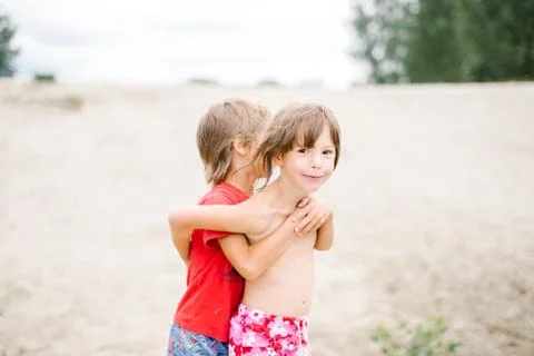 Fraternal twins hugging at the beach while playing on hot summer day Stock Photos