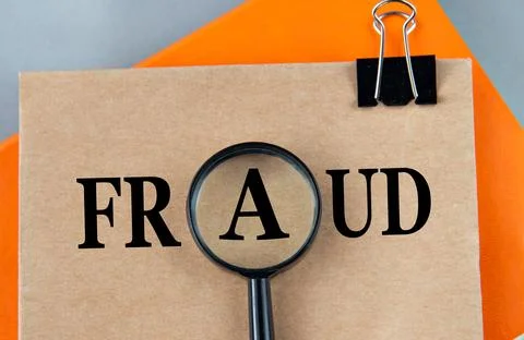 FRAUD - word on a brown sheet with a magnifying glass in the center Stock Photos