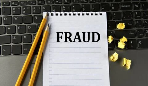 FRAUD - word in a white notepad on the background of a laptop with pencils Stock Photos