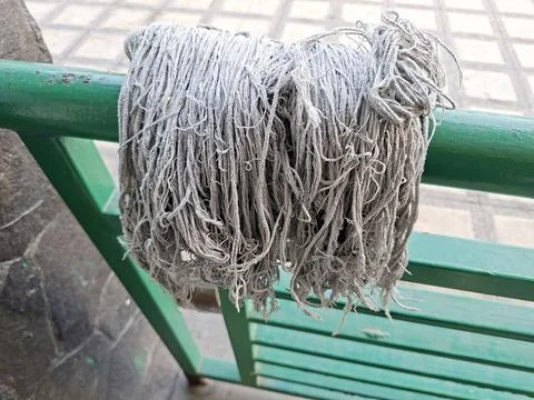 A frayed grey string mop head hanging over a green metal railing to dry out.. Stock Photos