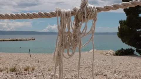 Frayed nautical rope stretched above a beach and waving gently in the wind .. Видео 333795716