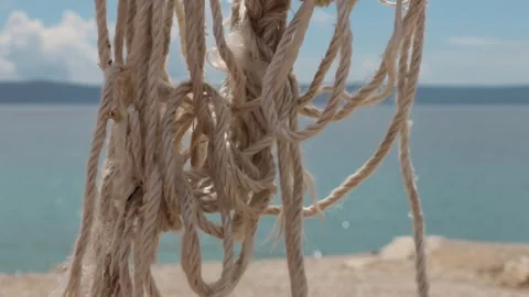 Frayed nautical rope stretched above a beach and waving gently in the wind .. Видео 333795744