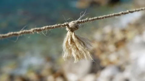 Frayed rope knot swaying gently in the breeze above a pebble beach by the sea Stock Footage 346799518