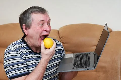Freak eats lemon while holding a laptop while sitting on the couch Stock Photos