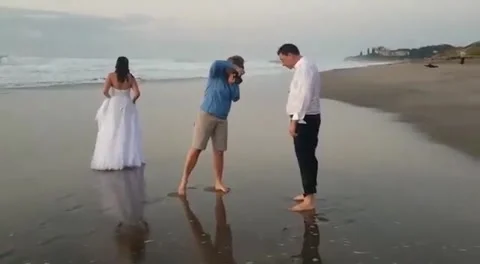 Freak wave knocks bride over on beach during photo shoot Stock Footage 272891174