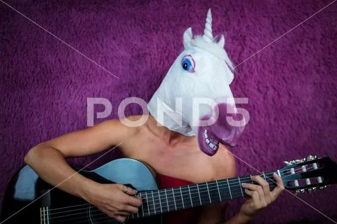 Freaky young woman in comical mask playing the guitar on the purple background Stock Photos