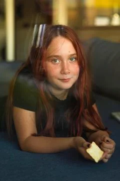 Freckled girl lying on a sofa by the window looking into the camera Stock Photos