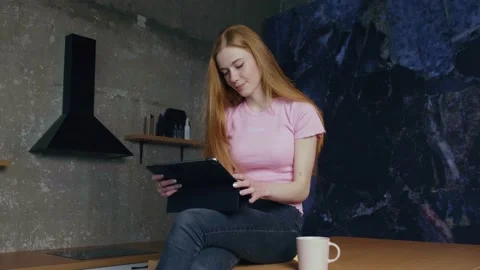 Freckled woman is using a tablet in the kitchen drinking a coffee while working Stock Footage 155752865