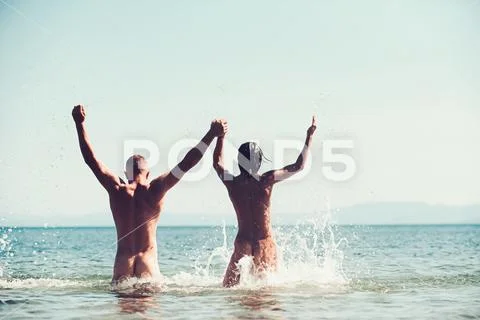 Free couple nudist swim on beach with arms up. Stock Photos