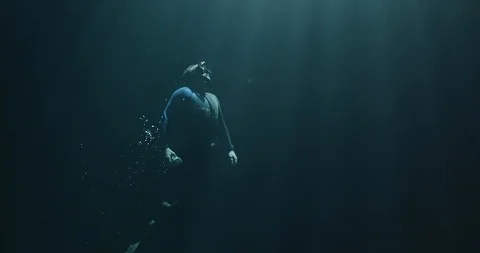 Free diver rises to the surface in a dark abyss in slow motion Stock Footage