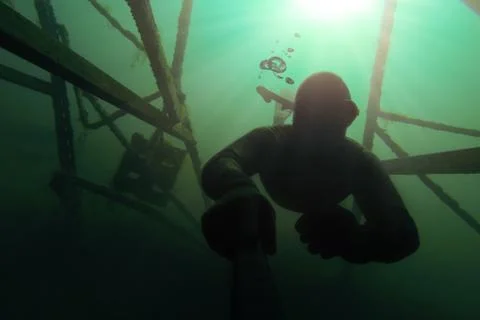 Freediver going deap in the water with a structure above him. Stock Photos