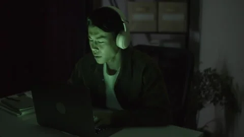 Freelance Developer Wearing Headphones Working on Laptop Late at Night Stock Footage 256981733