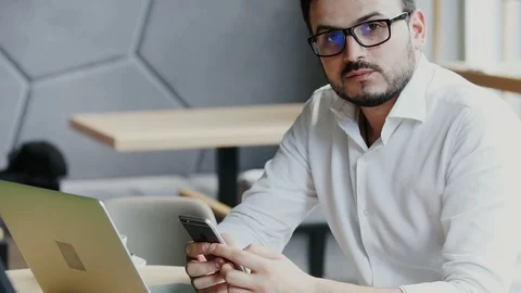 Freelance man with black glasses using phone and looking to the camera in casual Stock Footage 112987202