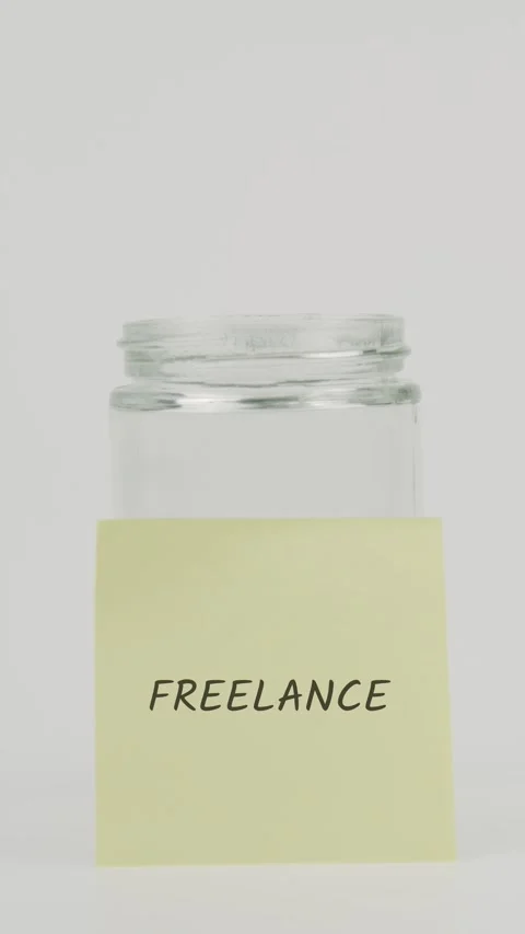 Freelance text or word on yellow sticky note attached to glass jar with hand Stock Footage 311736126